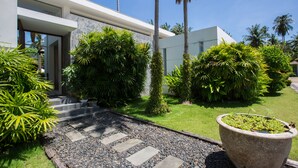 Una casa moderna con un camino de piedra que conduce a la entrada, rodeada de exuberante vegetación y palmeras.