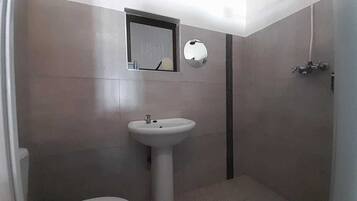 Un baño pequeño con inodoro, lavamanos pedestal, espejo y ducha.