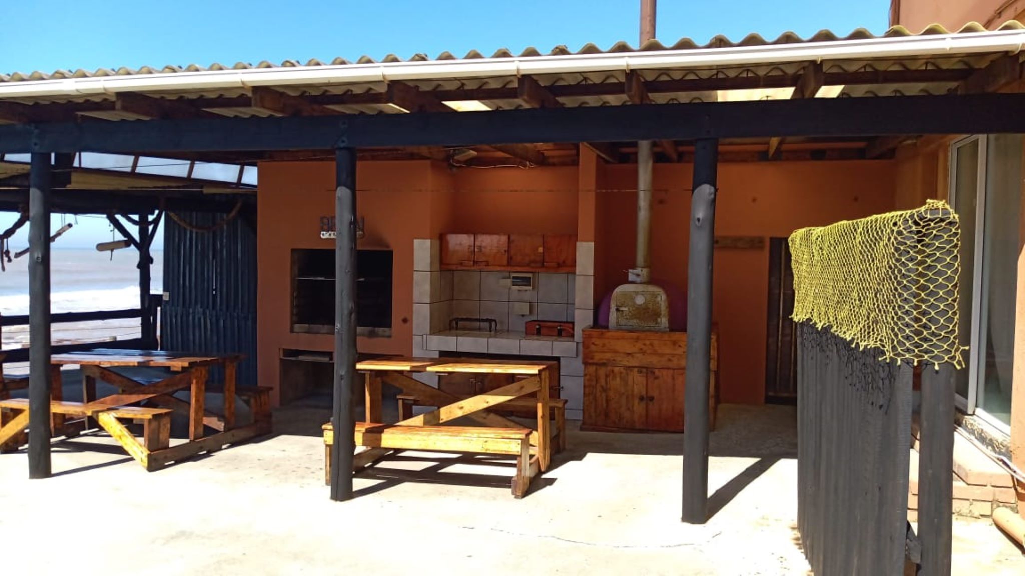 Un espace extérieur abrité comprenant une table et des chaises en bois, un barbecue et un coin cuisine avec des placards et une cuisinière.