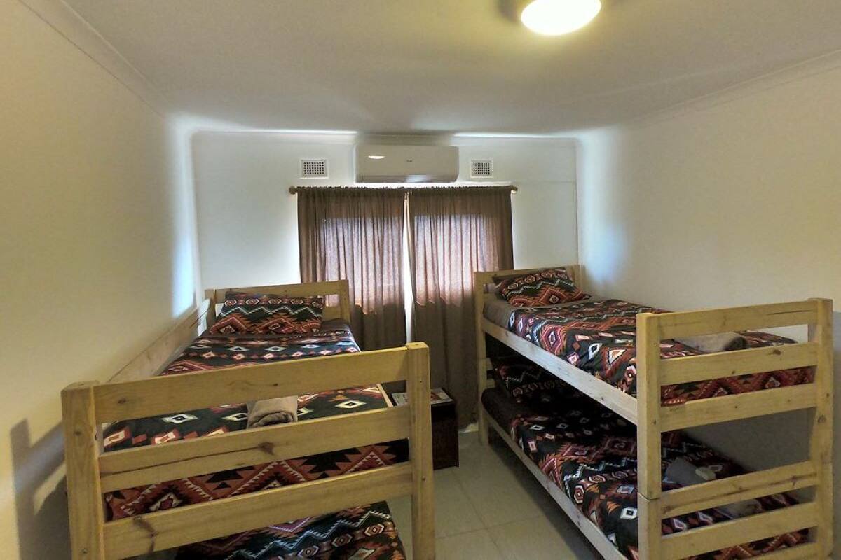 A dormitory room with two bunk beds, a ceiling fan, and a window with curtains.