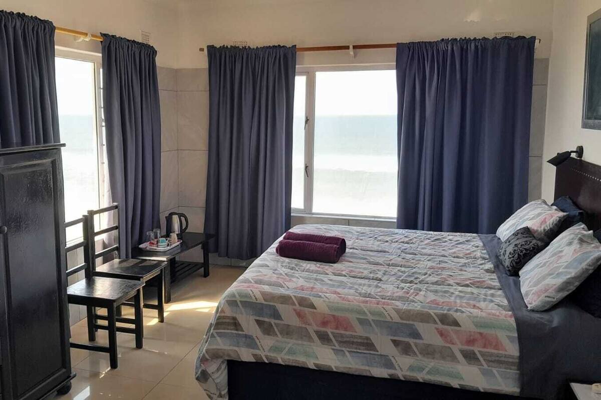 A hotel room with a bed, a desk, and a chair. There are curtains on the windows, and a television is mounted on the wall.