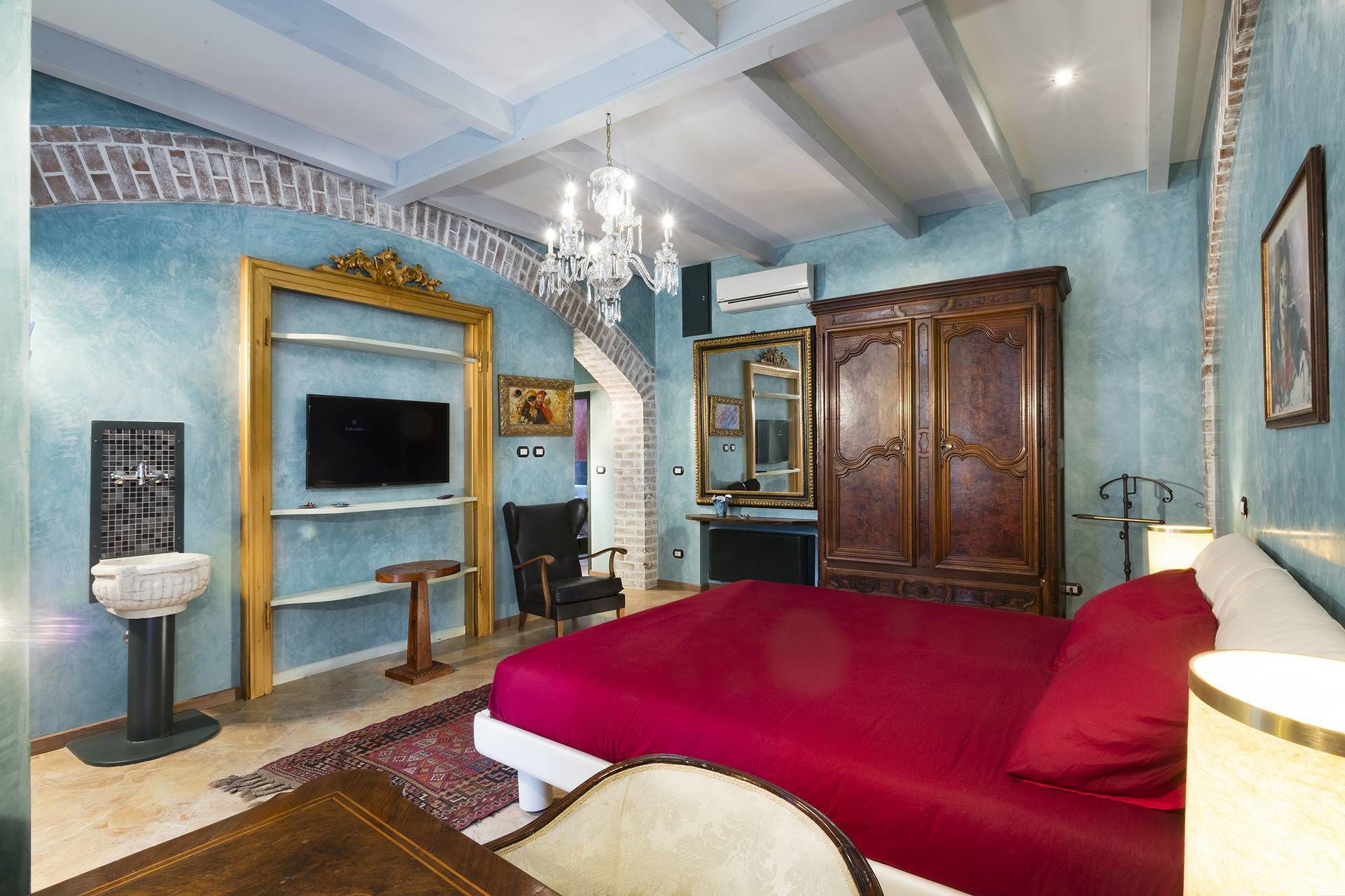 A bedroom with a large bed, a TV, a chandelier, and a wardrobe.