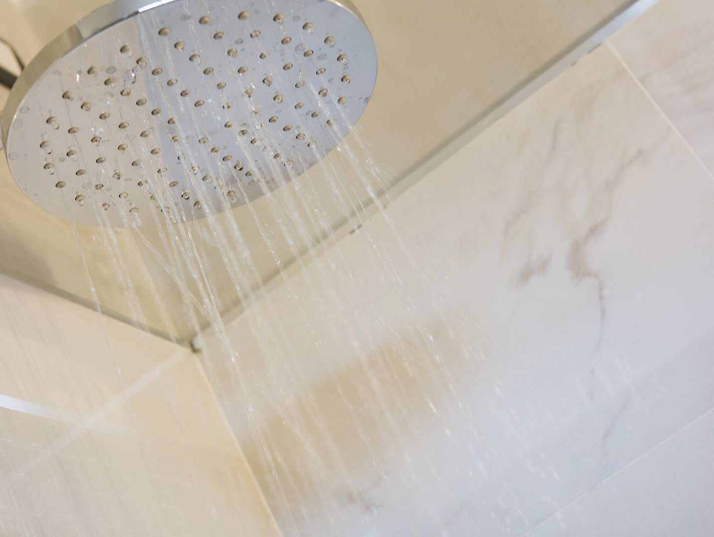 A showerhead with water flowing down a tiled wall.