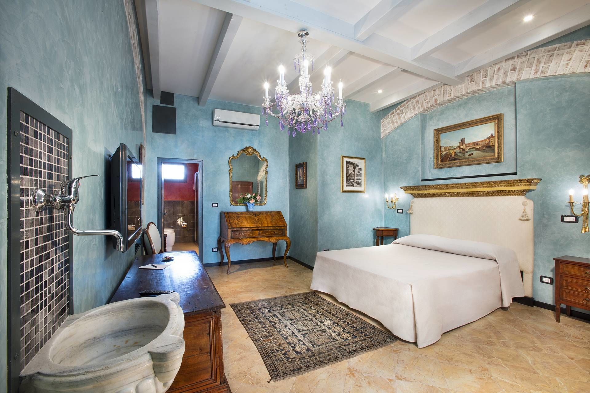 Una camera da letto con un letto grande, una scrivania in legno, un lavabo in marmo e un lampadario.