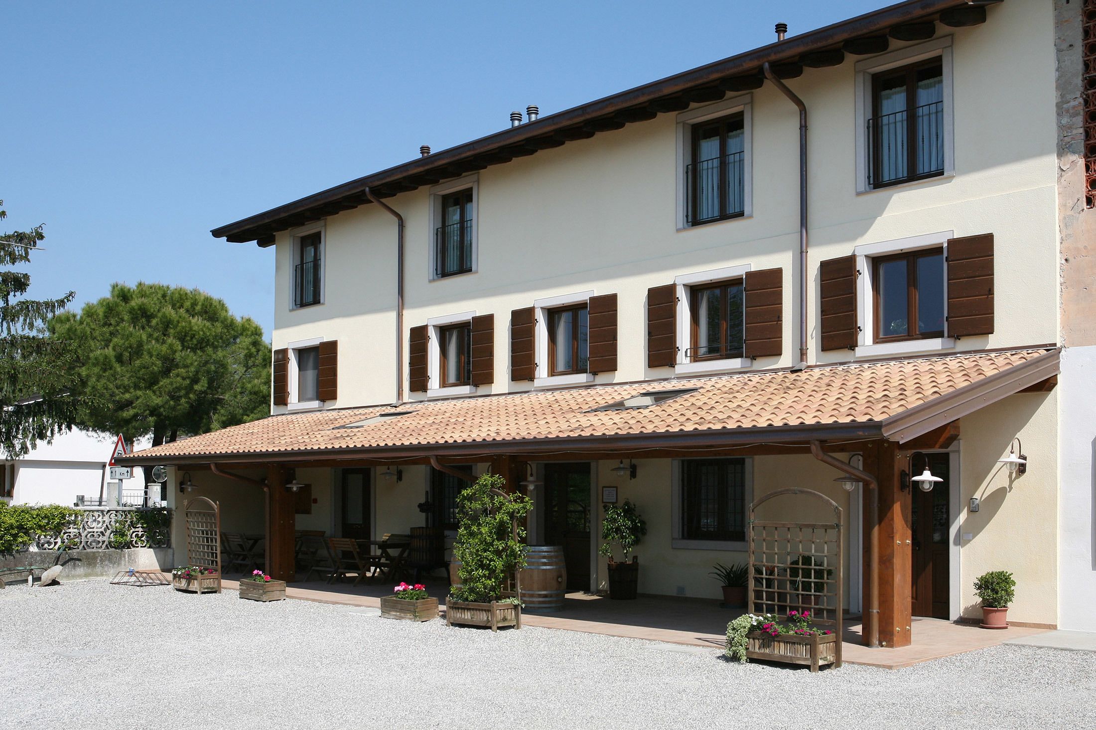 A two-story building with a tiled roof, multiple windows with shutters, and a covered porch area with potted plants.