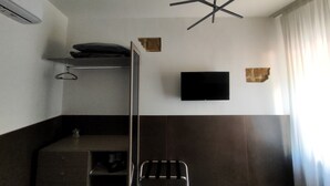 Una habitación compacta con una litera, un televisor de pantalla plana montado en la pared, una lámpara en el techo y una ventana con cortinas.