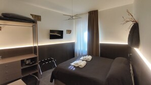 Una habitación de hotel moderna con cama, escritorio, silla, televisor de pantalla plana y ventana con cortinas.
