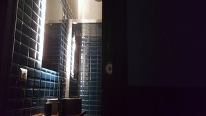 Baño con azulejos azul oscuro, un secador de manos y un dispensador de toallas.