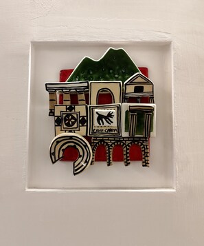 A decorative wall piece with a house, a dog, and a cave sign. - Cloister Inn (Naples)