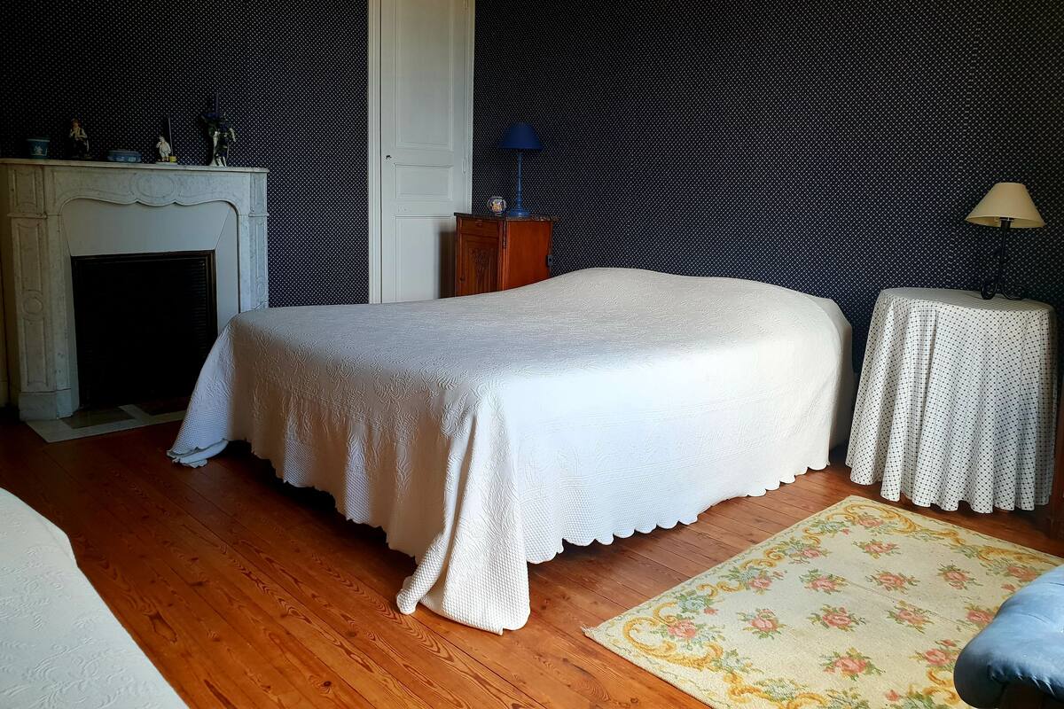 A bedroom with a bed, a nightstand, a lamp, a dresser, and a fireplace.