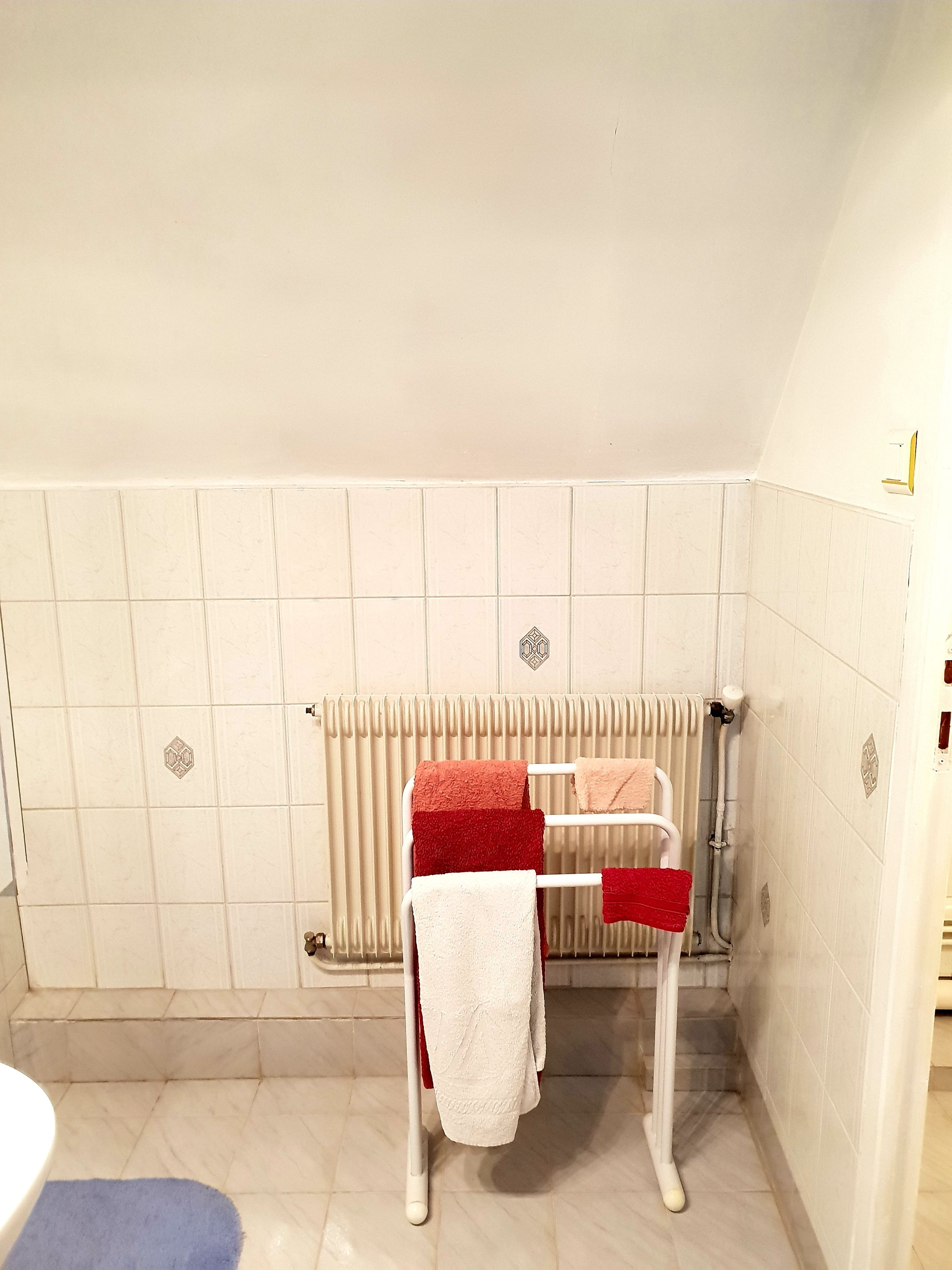 A bathroom with a white bathtub, a white towel rack with towels, and a white radiator.