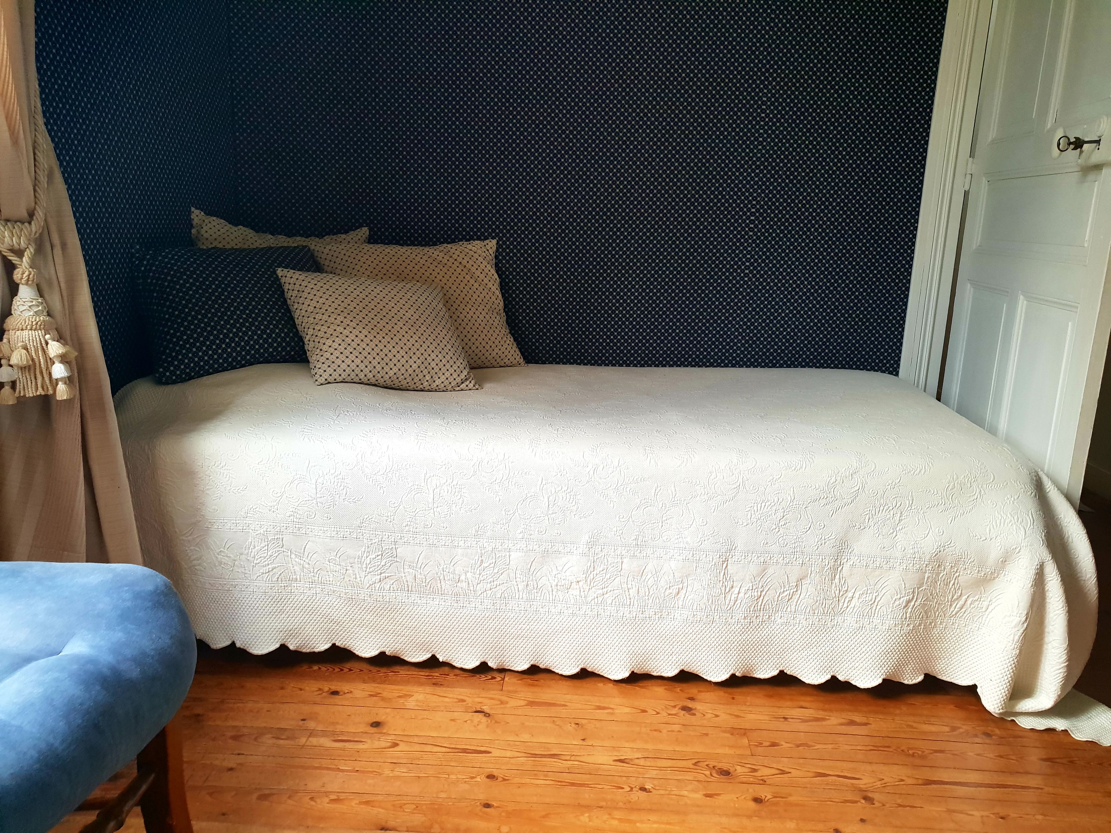 A bed with a white lace cover, a dark headboard, and a blue chair.