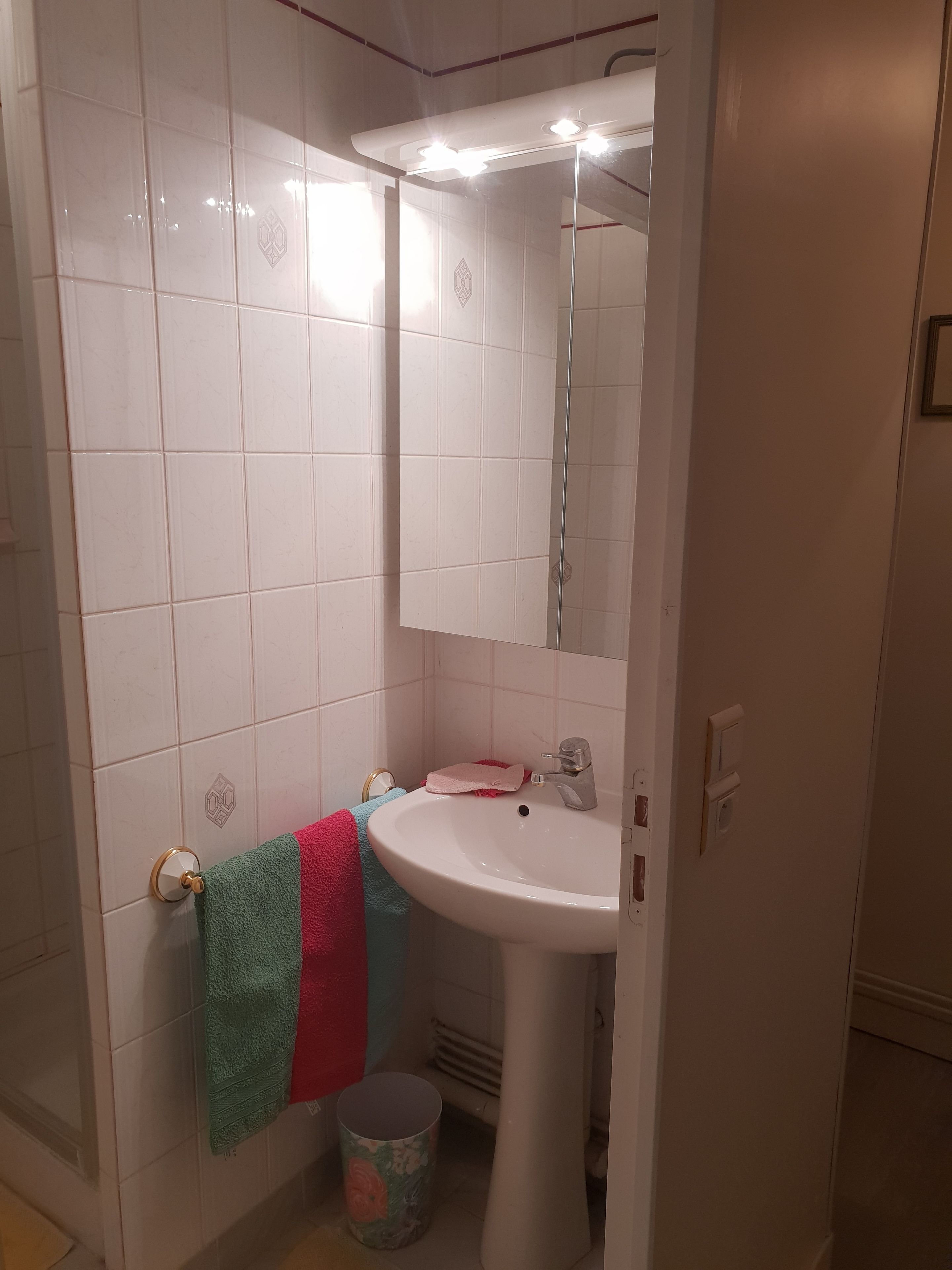 Ett badrum med vita kakelplattor, ett handfat, en spegel och en handdukshängare.