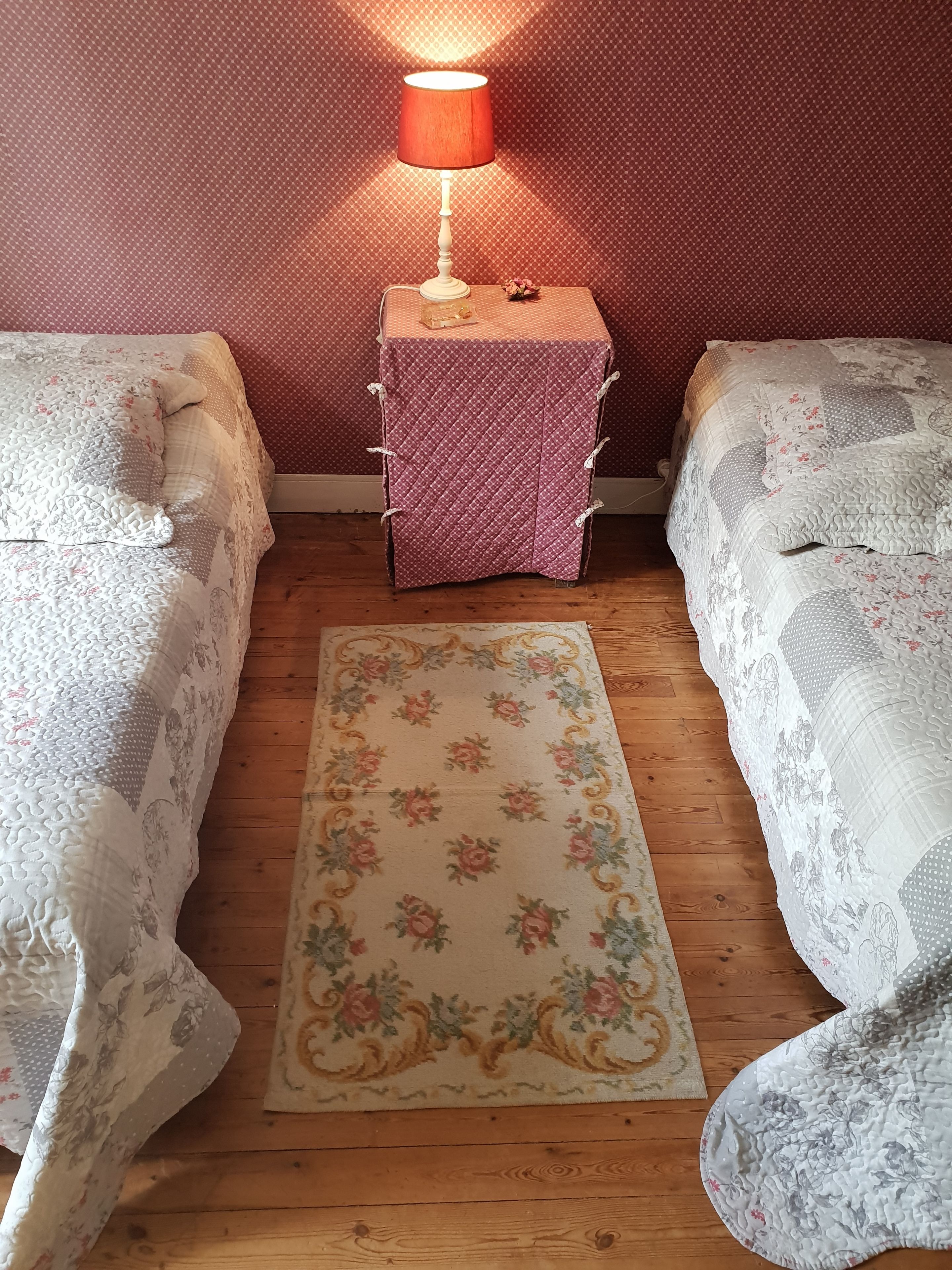 Une chambre avec deux lits, une table de chevet avec une lampe et un tapis à motifs floraux.
