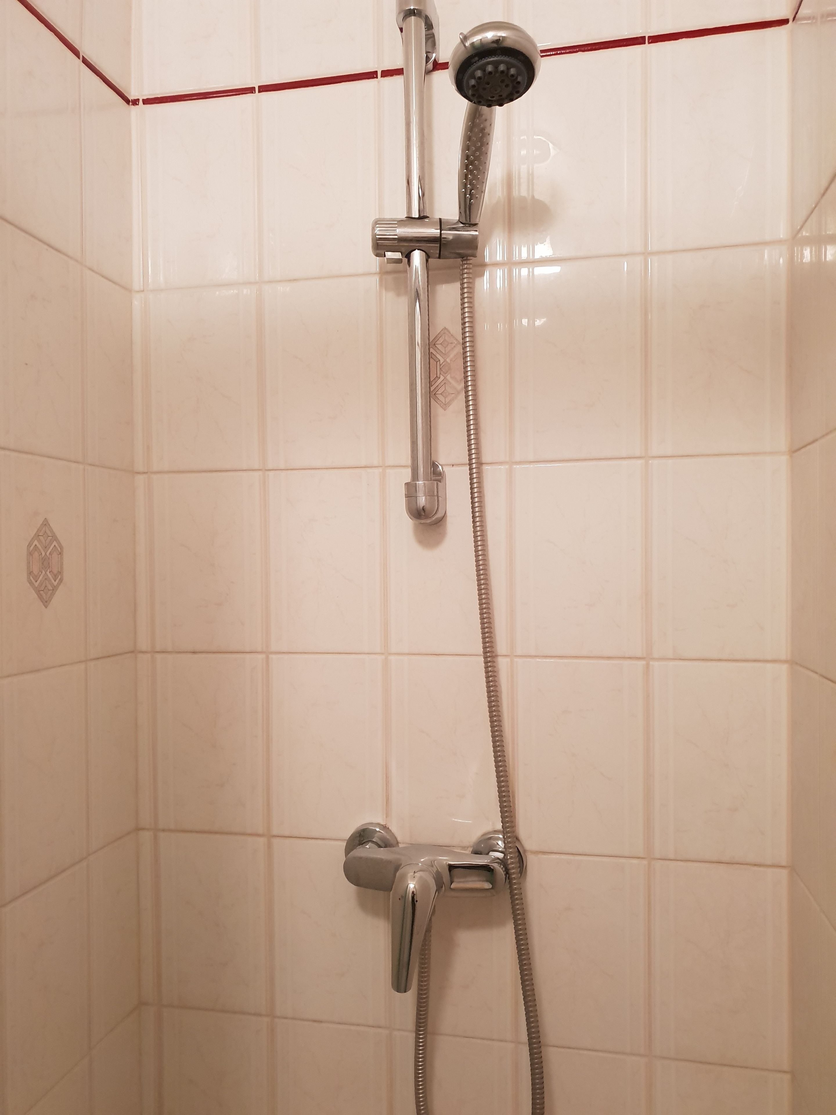 Une douche équipée d’un pommeau de douche à main et d’un robinet fixé au mur.