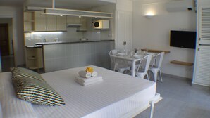 A hotel room with a bed, a small kitchenette, a dining area, and a TV.