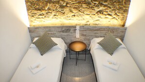 A room with two beds, a small table, and a textured wall.