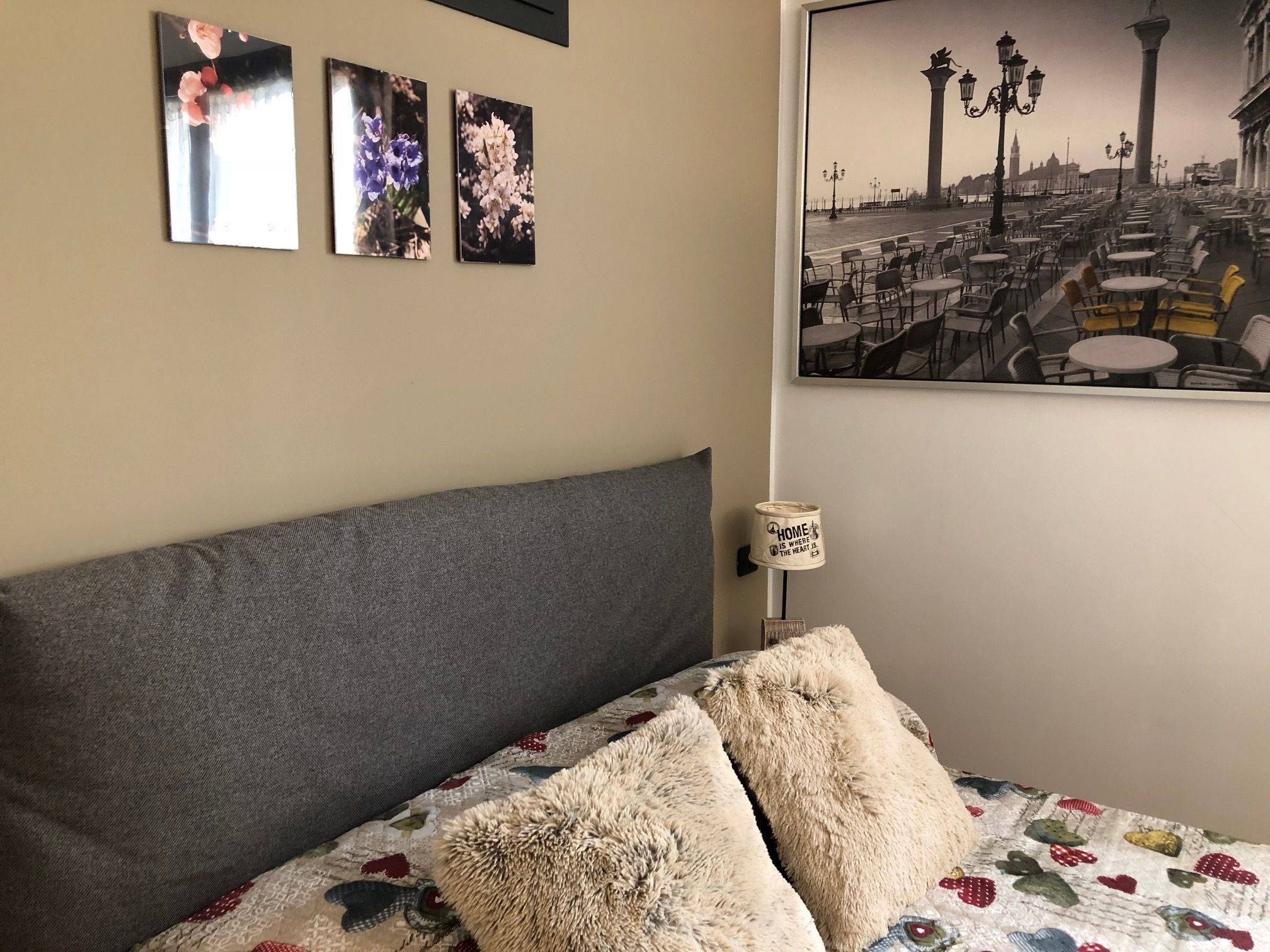 A bedroom with a large bed, a gray headboard, and a wall-mounted picture of a cityscape.
