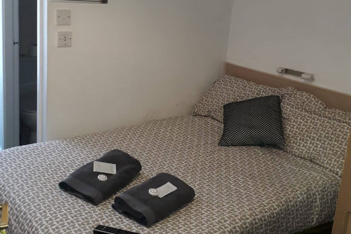 Cama bem arrumada com roupa de cama estampada, um travesseiro e duas toalhas dobradas com etiquetas.