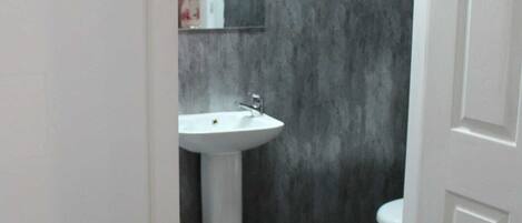 Un baño estrecho con lavamanos blanco, inodoro y espejo.