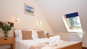 A bedroom with a wooden bed, a nightstand with a vase of flowers, a wall-mounted picture, and a skylight.