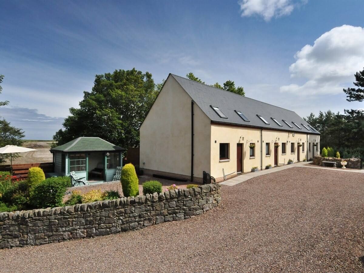 A building with a sloped roof, a stone wall, and a gravel driveway.