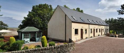 A building with a sloped roof, a stone wall, and a gravel driveway.