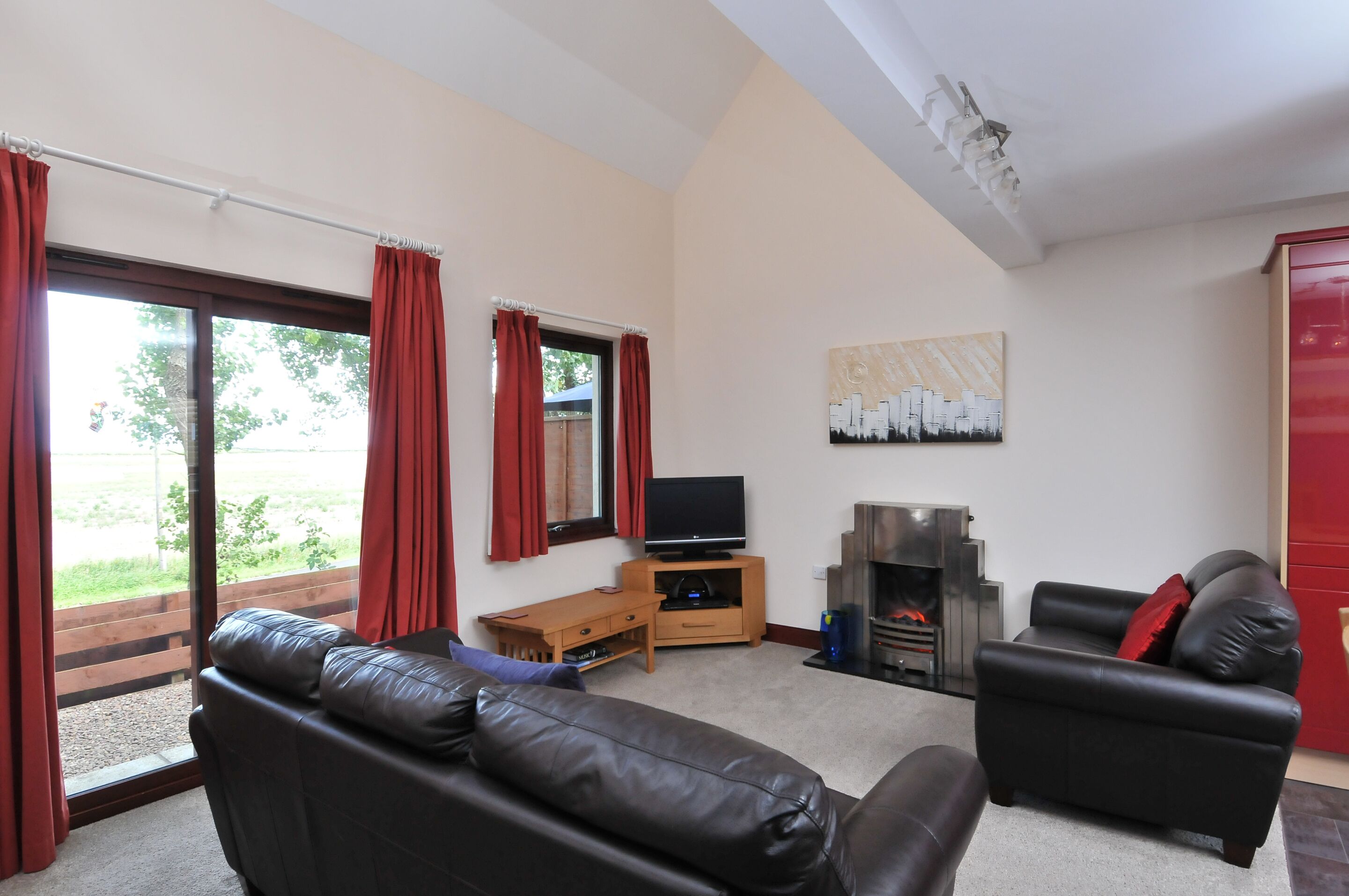 A living room with a sofa, a television, a fireplace, and a red door.