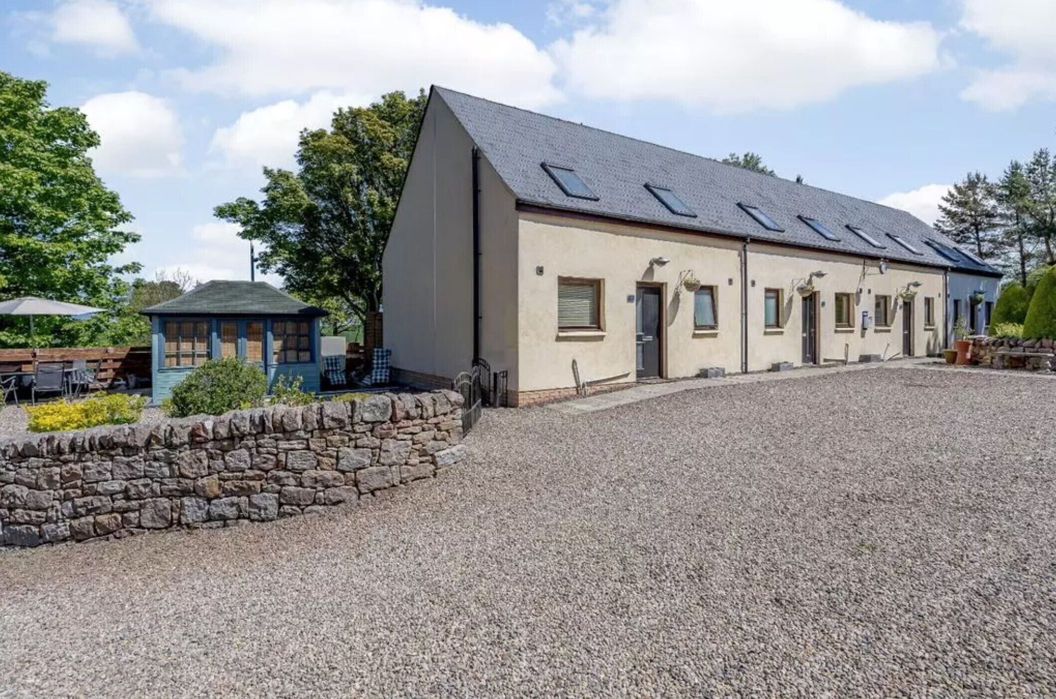 A building with a sloped roof, a stone wall, and a gravel driveway.