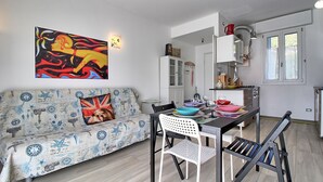 A modern living room with a sofa, dining table, and chairs. There is a painting on the wall, a cabinet, and a window. - Logicasa Zazzi House (Como)