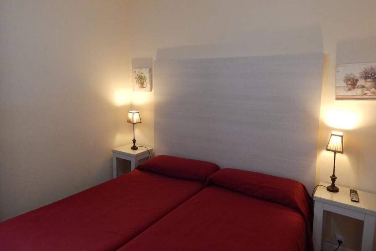 A bedroom with two beds, each with a red bedspread, and bedside lamps.
