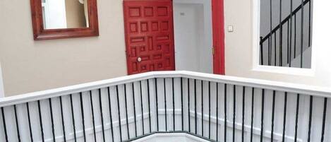 Una escalera con barandilla blanca y una puerta roja al fondo.