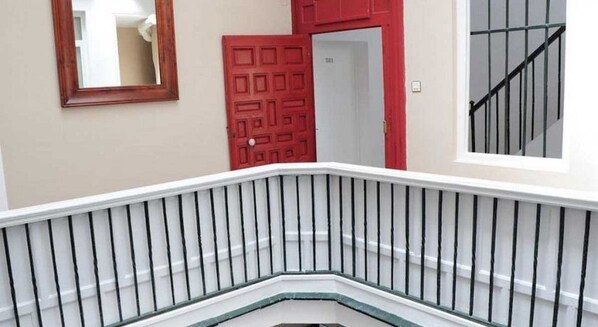 A staircase with a white railing and a red door in the background.