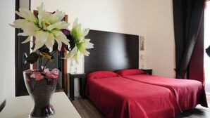 Een hotelkamer met een bed, een nachtkastje, een vaas met bloemen en een donker hoofdeinde.