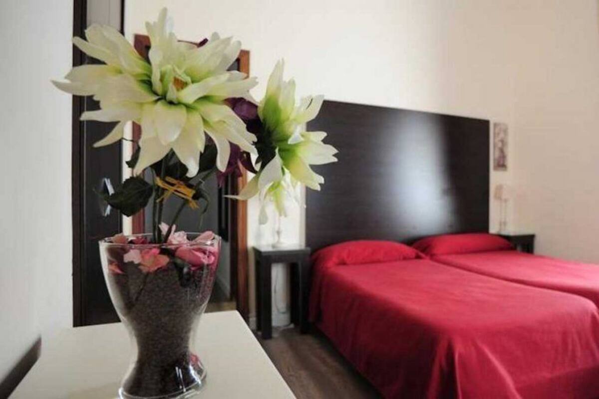A hotel room with a bed, a nightstand, a vase with flowers, and a dark headboard.