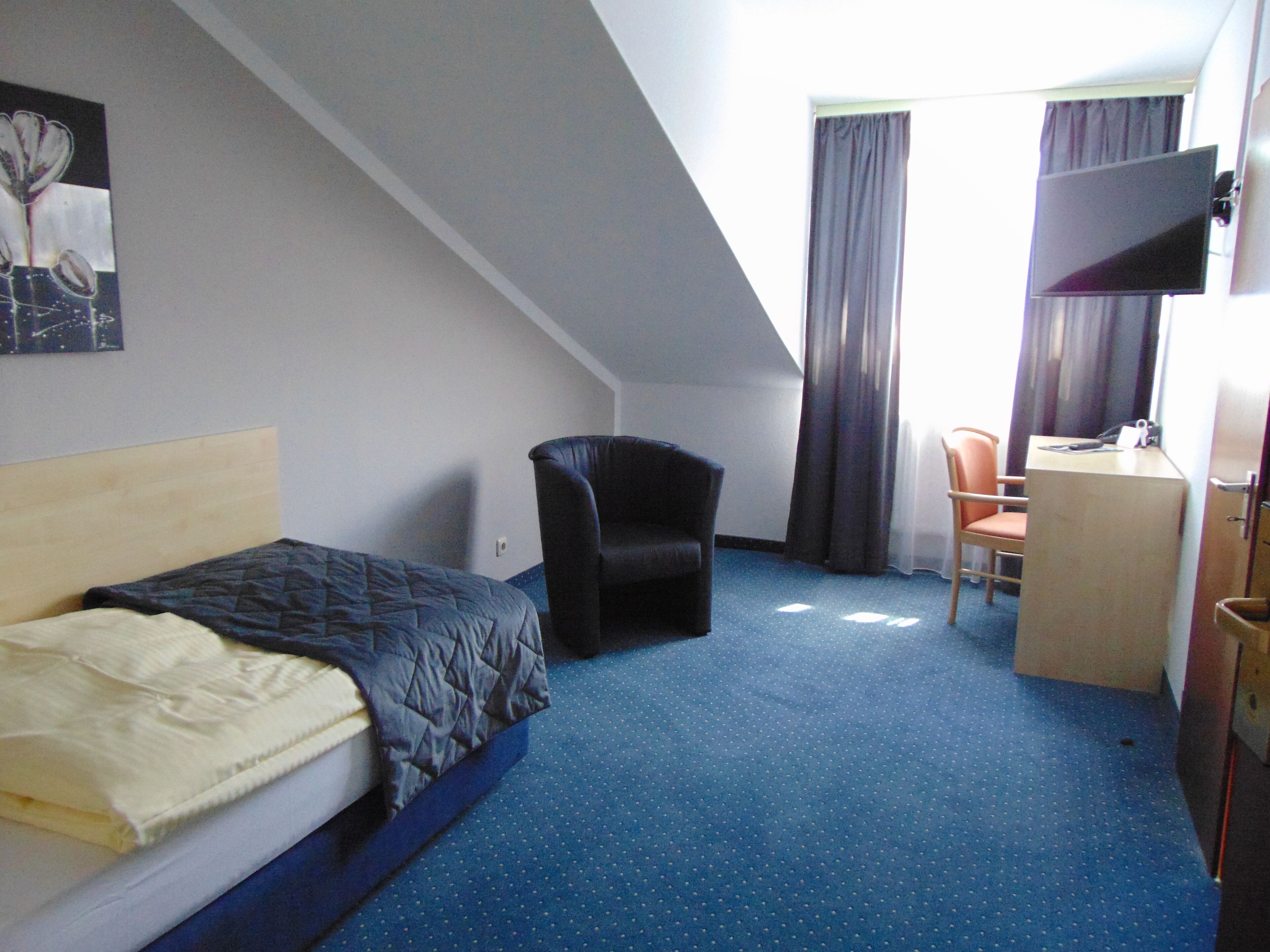 Une chambre d’hôtel avec un lit, un bureau, une chaise et une grande fenêtre avec des rideaux.
