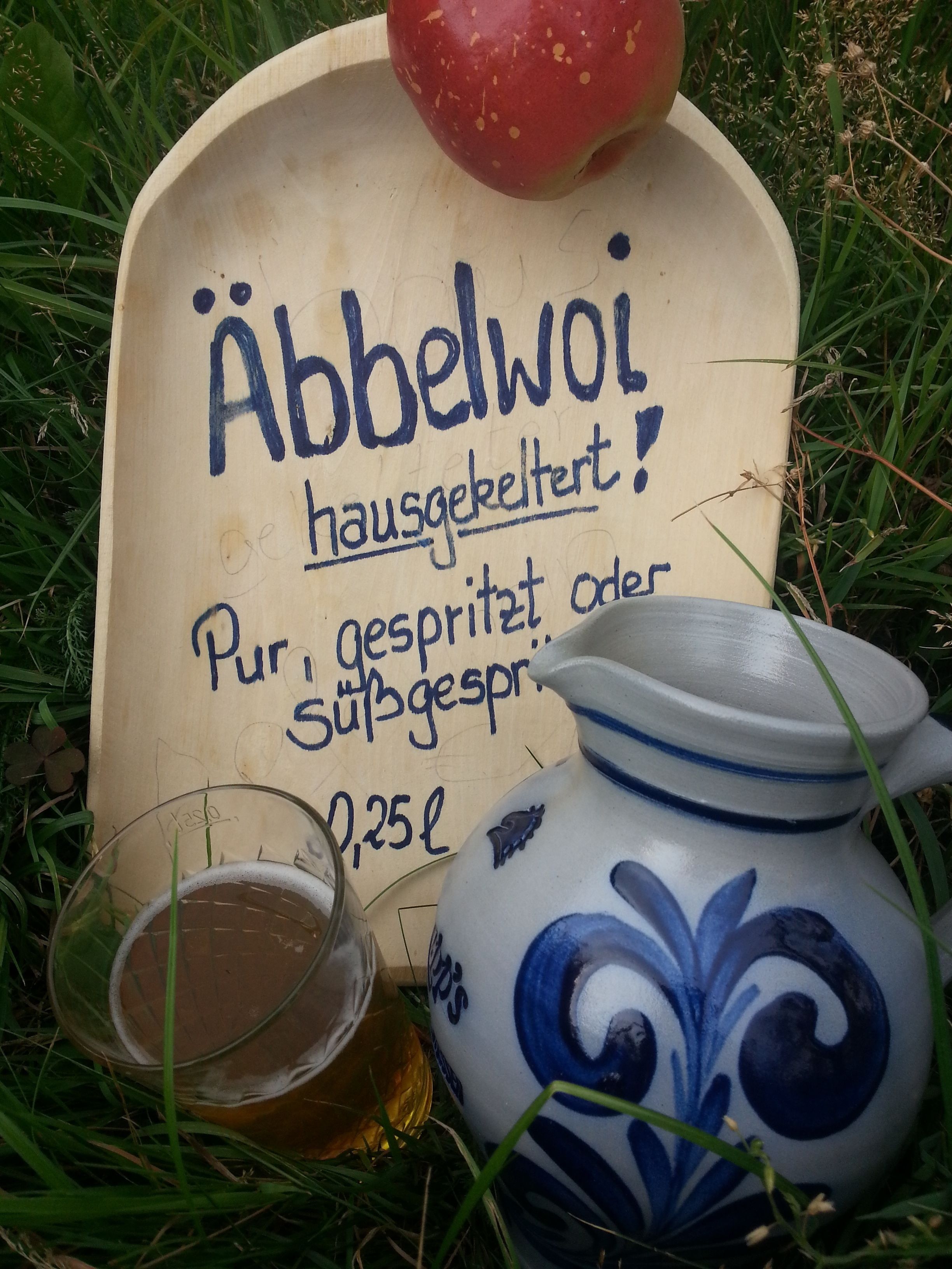 A wooden sign with text, a glass with a liquid, and a ceramic jug.
