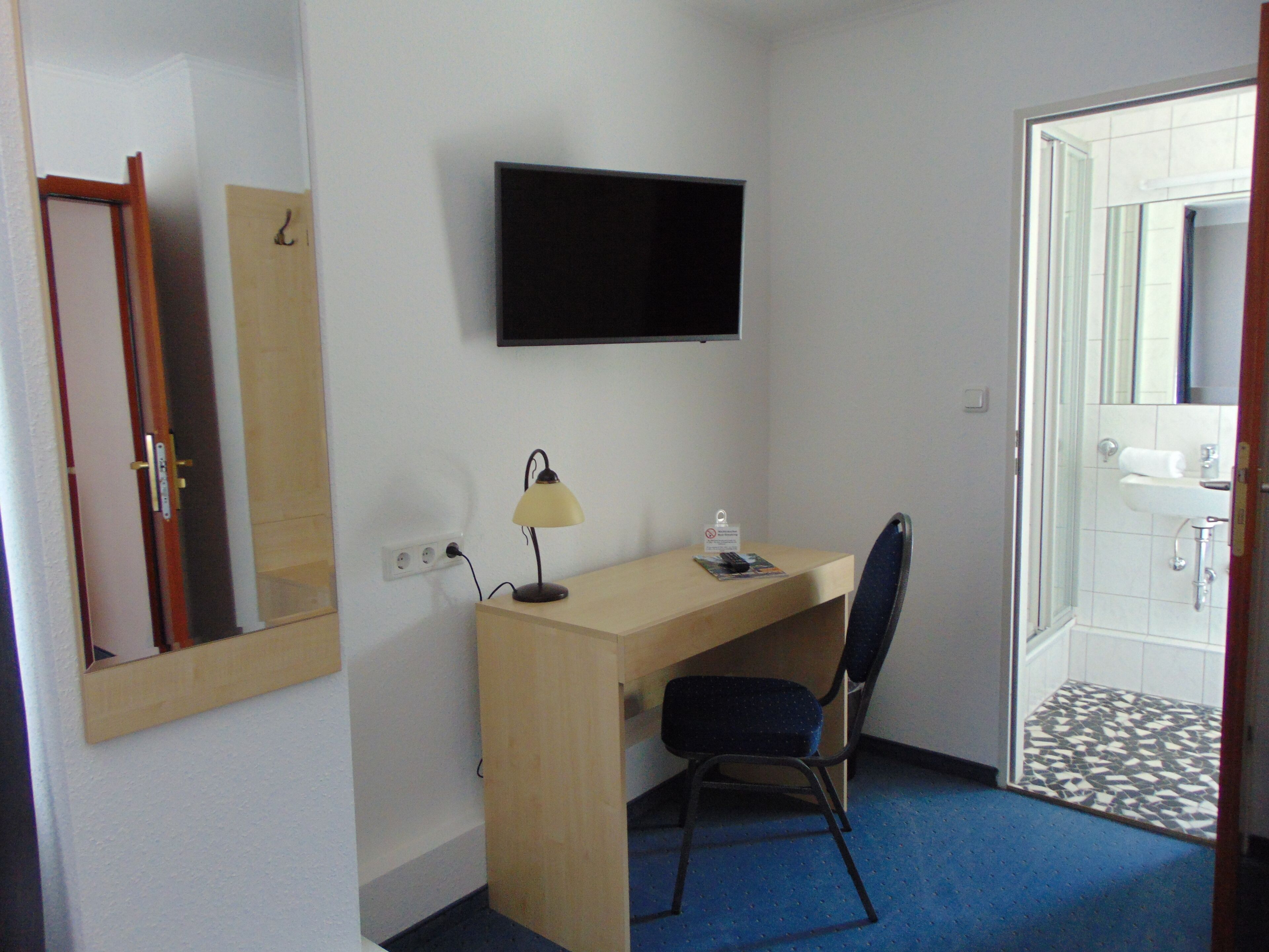 Una habitación de hotel pequeña con escritorio, silla, televisor y baño con piso de baldosas.
