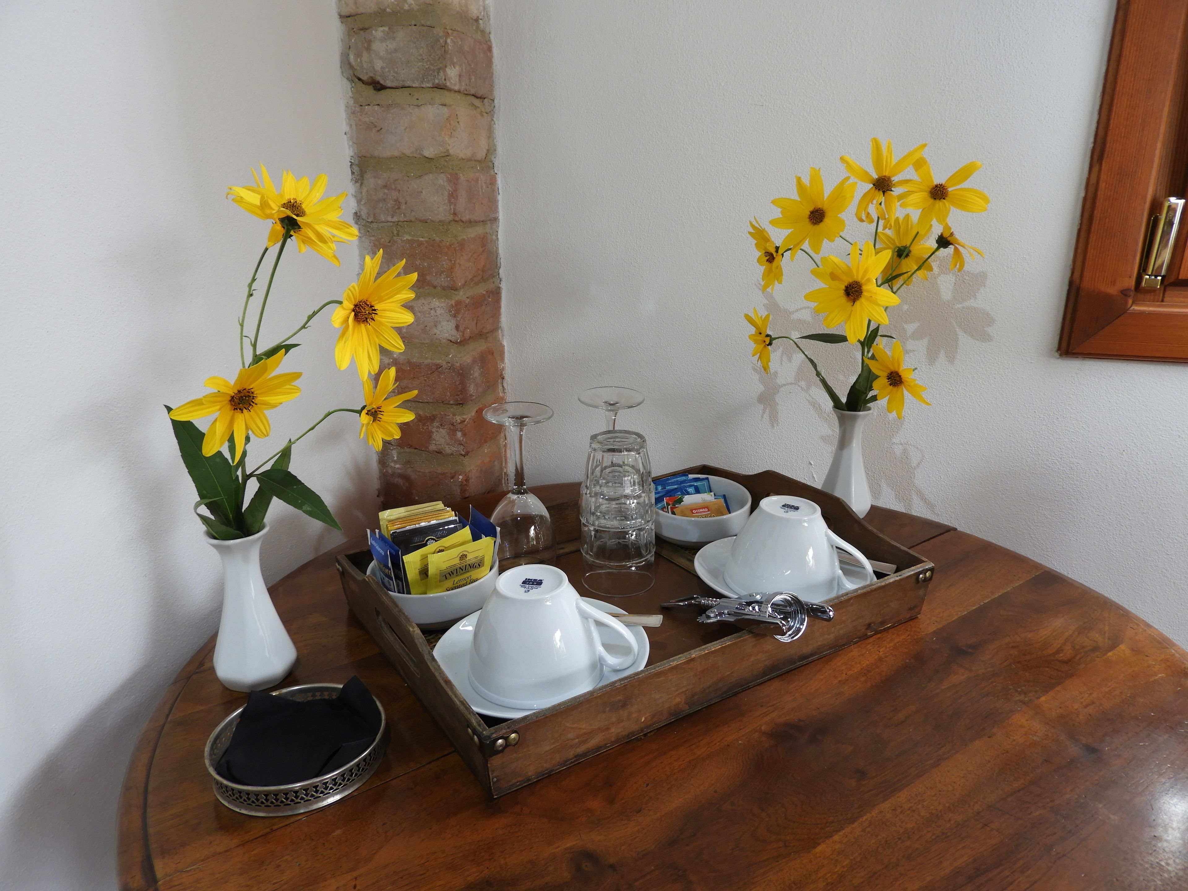 A wooden tray with white teapots, a glass, and a tray of snacks on a round table.