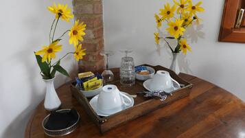 A wooden tray with white teapots, a glass, and a tray of snacks on a round table.