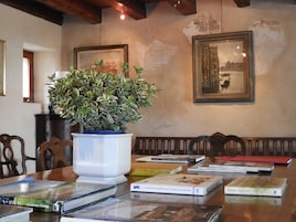 Un comedor con una mesa de madera, libros, una planta en maceta y dos cuadros en la pared.