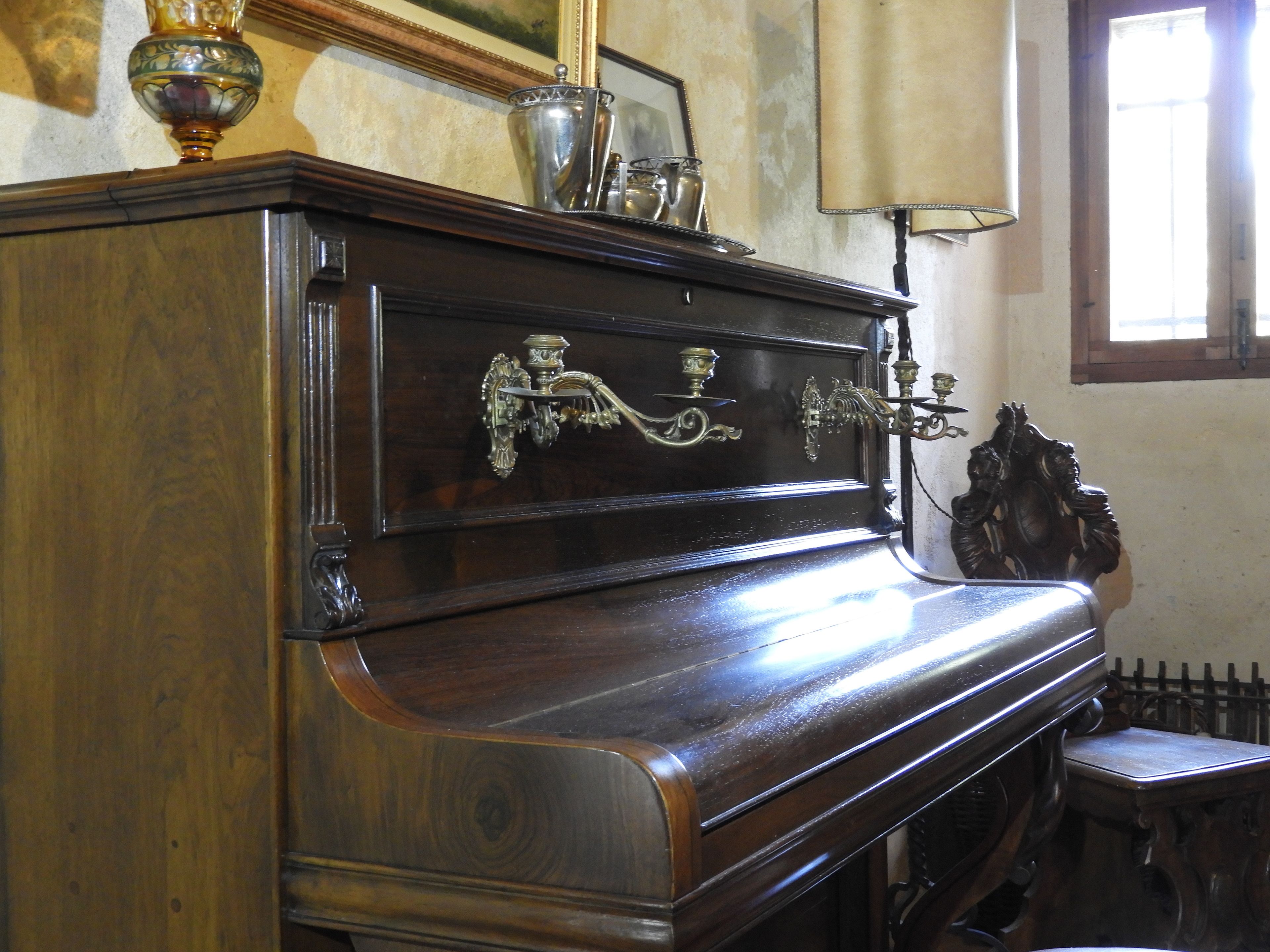 Een antieke, klassieke piano met decoratieve metalen details en een houten afwerking.