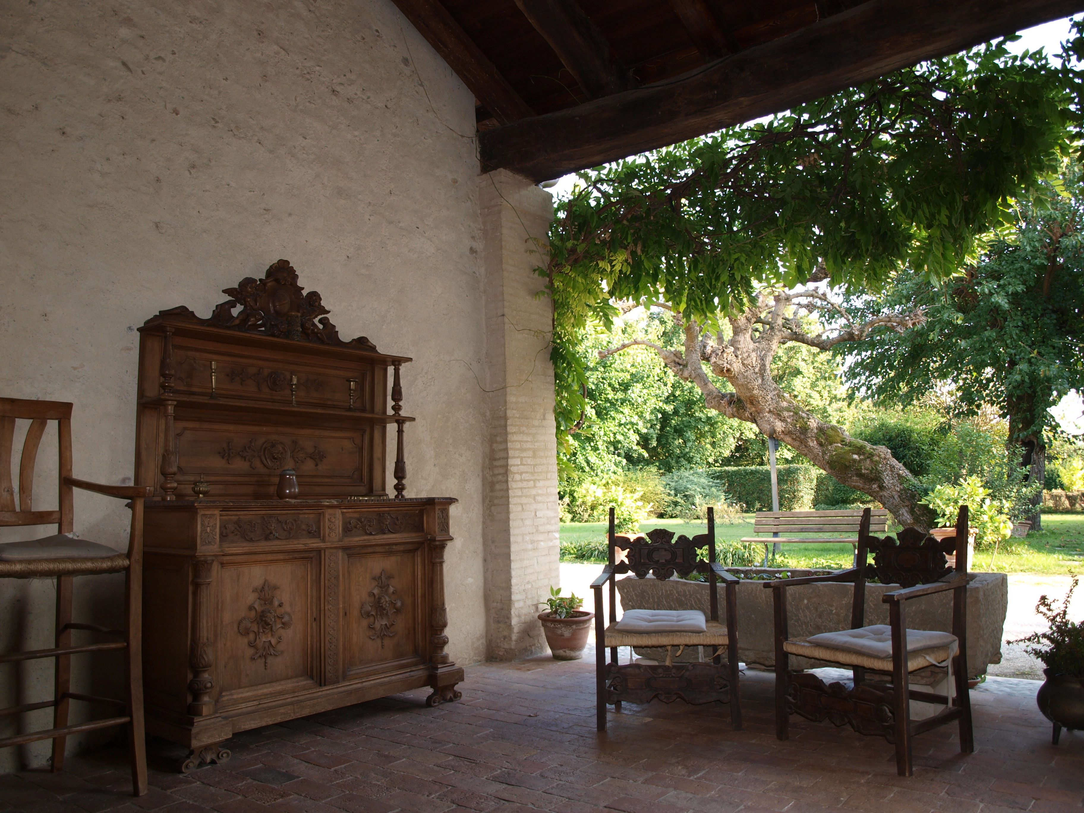 Un patio rústico con un banco, una mesa y un gran aparador de madera tallada.