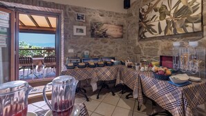 A breakfast setup with a stone wall, a table with a plaid tablecloth, and a view of the outdoors. - B&B Amoliv (Cavriglia)