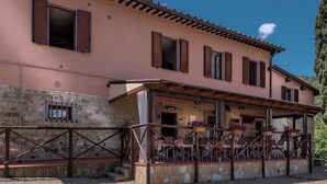 A two-story building with a stone facade, wooden shutters, and a covered outdoor seating area with tables and chairs. - B&B Amoliv (Cavriglia)