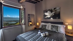 Un dormitorio con un ventanal grande, una cama con almohadas, una lámpara de noche y un cuadro de una flor.