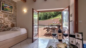 A room with a bed, a dining table with wine glasses and a bottle, and a view of an outdoor patio. - B&B Amoliv (Cavriglia)