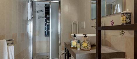 A bathroom with a glass shower enclosure, a sink with a mirror, and a shelf with toiletries.