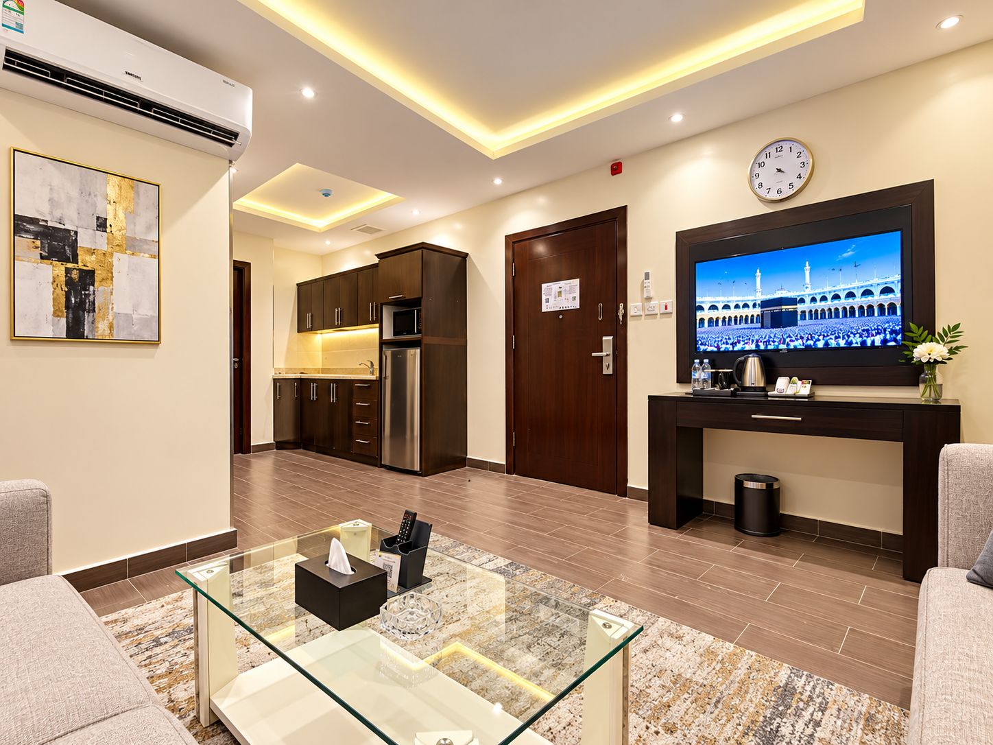 A hotel lobby with a modern kitchen, a flat-screen TV displaying a view of a mosque, and a reception desk.