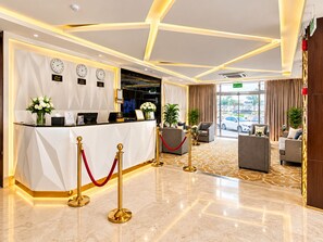 A hotel reception area with a reception desk, clocks, and a view of the street.